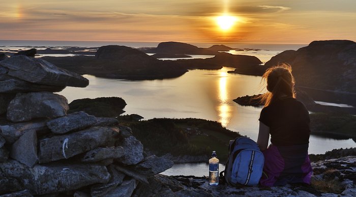 Jente sitter på fjelltopp og ser utover Flatanger og Flatanger Camping i solnedgang. Namdalen. Foto: Flatanger Camping.